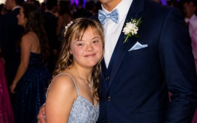 Il quarterback stella della squadra ha chiesto a mia figlia con la sindrome di Down di ballare al ballo di fine anno e, per un brevissimo istante, ho pensato che gli anni di bullismo fossero finalmente finiti. Poi ho trovato una chiavetta USB nascosta nella tasca del suo smoking. Dentro c’erano foto di mia figlia scattate nei suoi momenti più umilianti: mentre piangeva da sola in un bagno, stringendo la giacca strappata dopo essere stata presa di mira dai bulli, abbracciando il suo orsacchiotto di peluche mentre gli altri studenti ridevano alle sue spalle. Accanto alle foto c’era una busta rossa con quattro parole agghiaccianti scritte sopra: “DOPO CHE AVRANNO RISSO”. Quando ho allungato la mano per prenderla, il ragazzo che tutti chiamavano eroe mi ha afferrato il polso e mi ha sussurrato freddamente: “Stai zitta per il bene di tua figlia… o te ne pentirai”. Dall’altra parte della sala da ballo, mia figlia Rosie sorrideva più radiosa di quanto non la vedessi da anni, completamente ignara che la sua serata da sogno stava per trasformarsi in un incubo. Poi il capitano della squadra di football salì sul palco, inserì la chiavetta USB nel proiettore della scuola e guardò dritto mia figlia prima di dire: “Ragazzi, c’è qualcosa di importante che dovete sapere su Rosie.” Mi feci largo tra la folla, con il cuore che mi batteva forte. “Steven, fermati!” Ma i suoi compagni di squadra mi bloccarono la strada. La prima foto apparve sul grande schermo. Poi un’altra. E un’altra ancora. Ognuna immortalava uno dei momenti più crudeli della vita di mia figlia. Nella stanza calò il silenzio. Il sorriso di Rosie svanì lentamente. Pensavo di sapere esattamente cosa stesse per succedere. Pensavo che fosse tutta una messa in scena per umiliarla davanti a tutta la scuola. Ma poi Steven si mise una mano in tasca, tirò fuori qualcosa che non avevo mai visto prima e pronunciò una sola parola che quasi mi fece cadere in ginocchio… continua nei COMMENTI